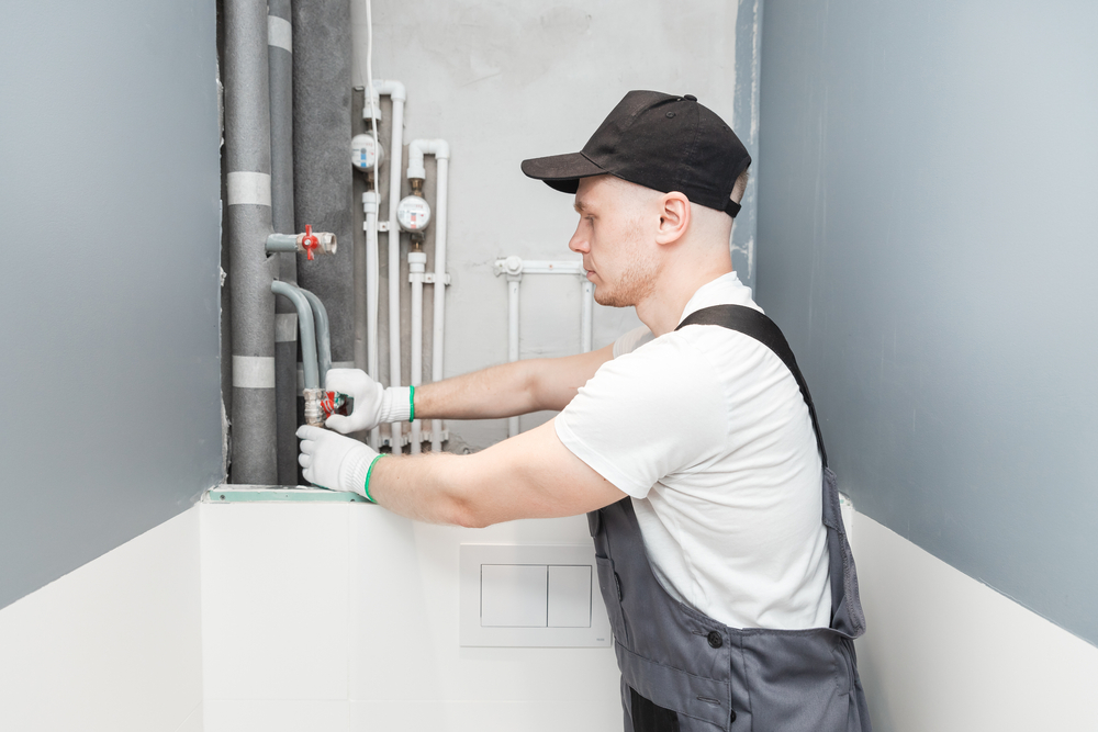 Male plumber checks pipes for central hot water systems and cold water supply of an apartment